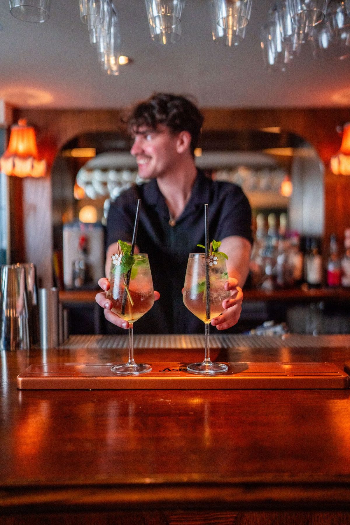 A bartender holding up two spritzes behind the bar