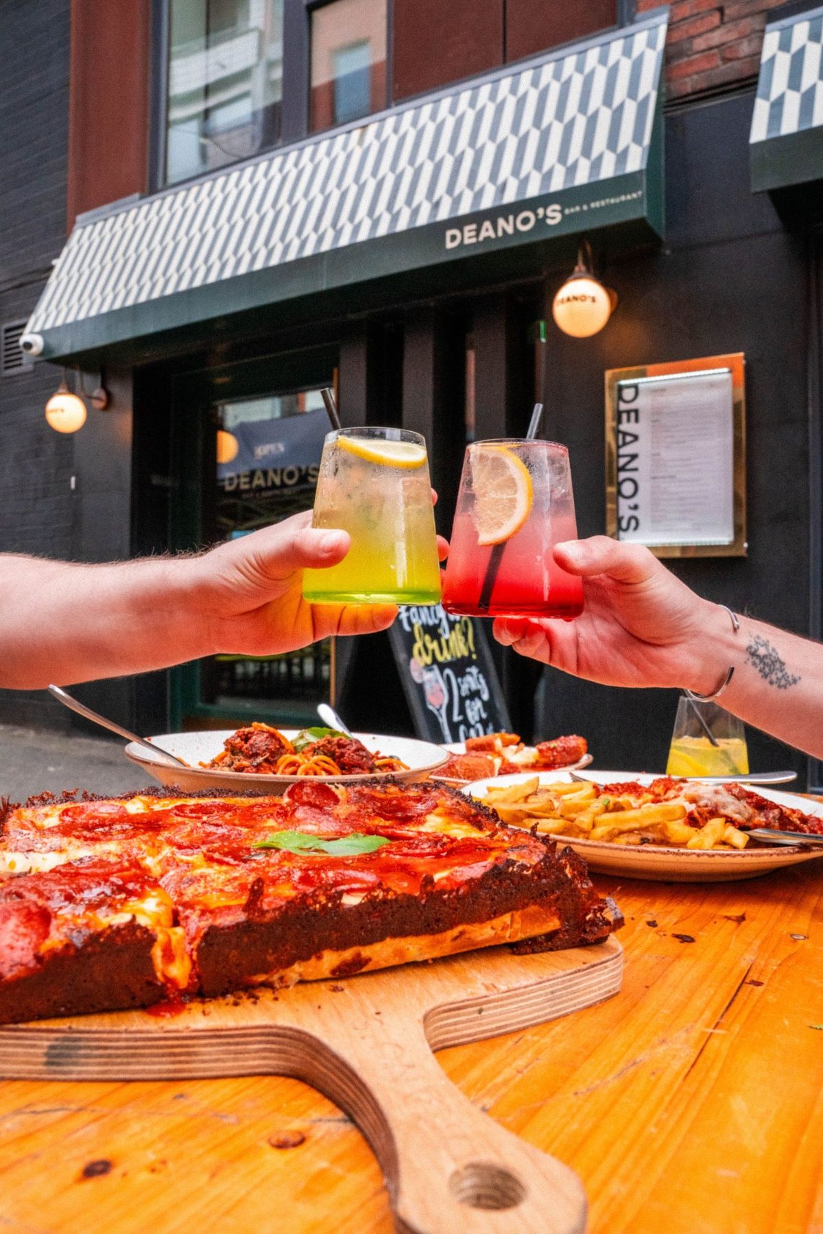Two drinks raised outside Deano's on Edge Street, over a deep-dish pepperoni pizza
