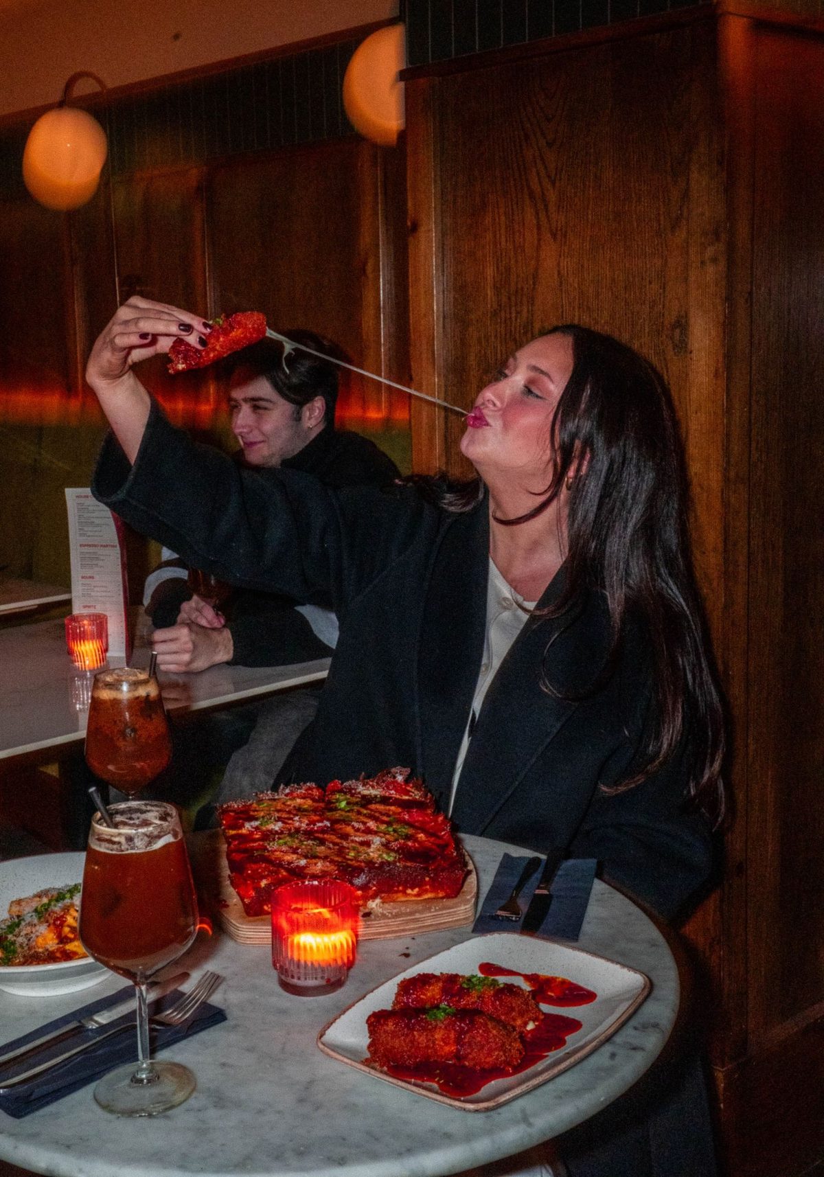 A guest at a booth stretching cheese from a mozzarella stick, deep-dish pizza and drinks on the table