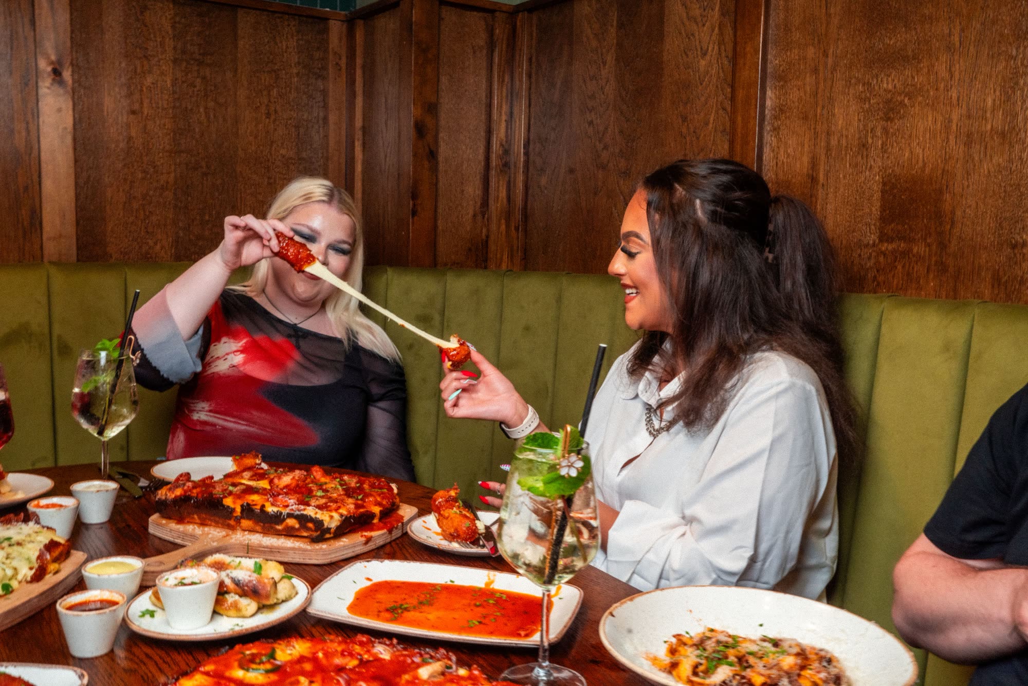 Two guests sharing pizza and pasta at a booth