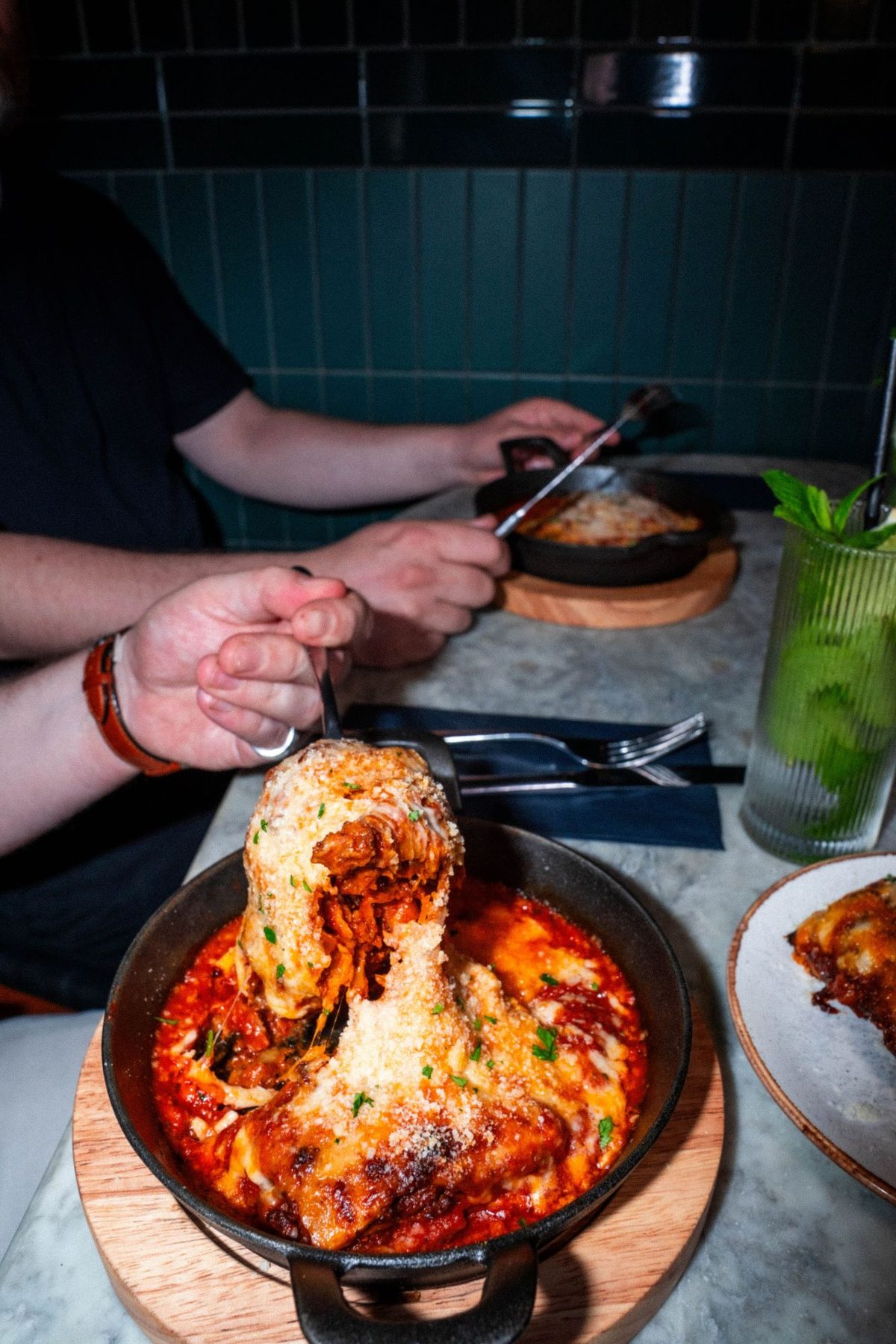 A forkful lifted from a cast-iron dish baked under melted cheese, the cheese stretching